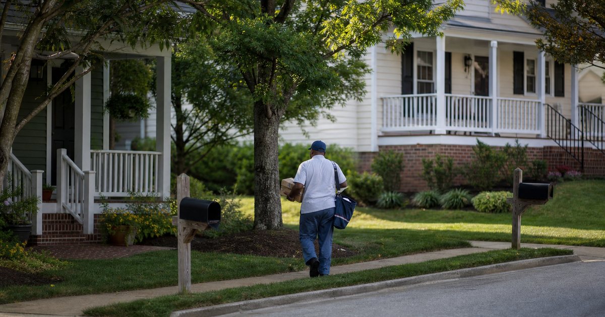 Residential street corner in a US suburb with a mail carrier delivering packages to two neighboring houses, mailbox posts, trees, clear afternoon light